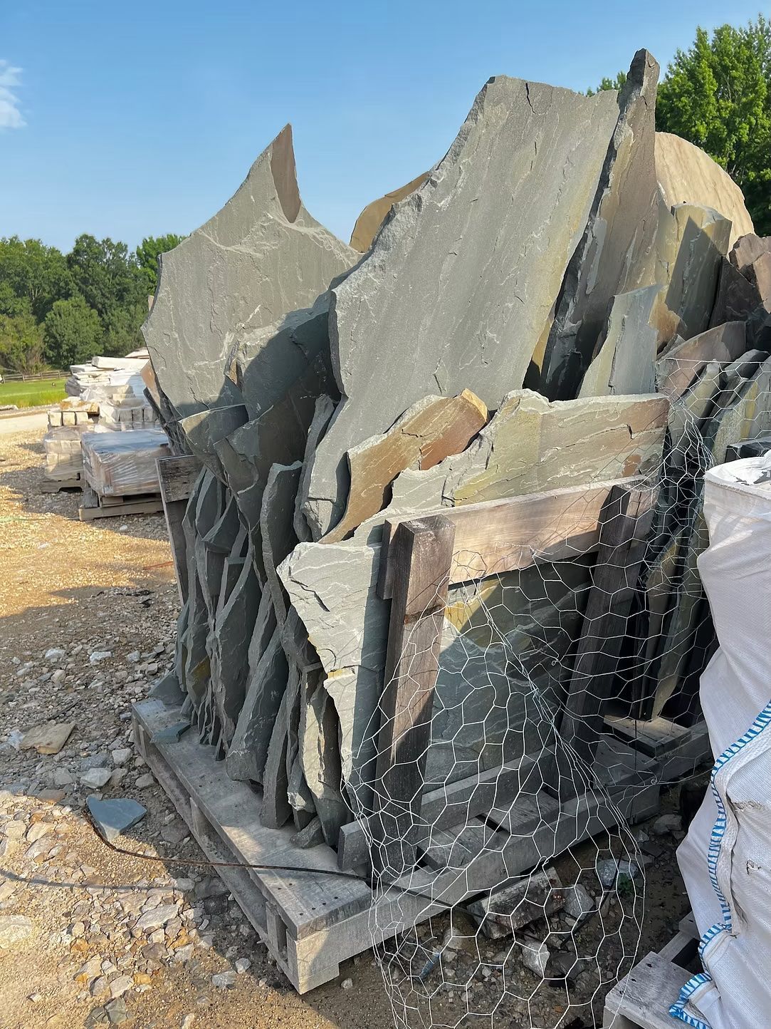 Pile of irregularly shaped gray and tan flagstone on a wooden pallet, outdoors.