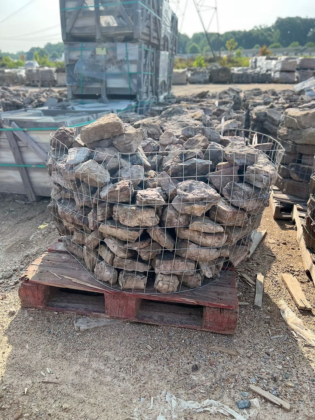 Stack of rough, gray bricks in a wire basket on a wooden pallet outdoors.