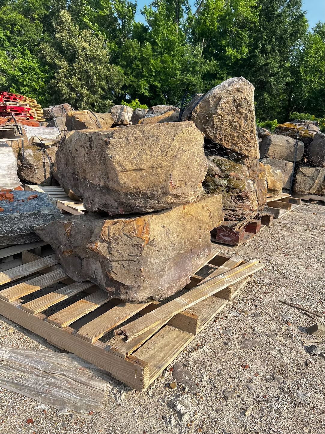Large, rough-hewn stone blocks stacked on a wooden pallet outdoors, likely for landscaping.