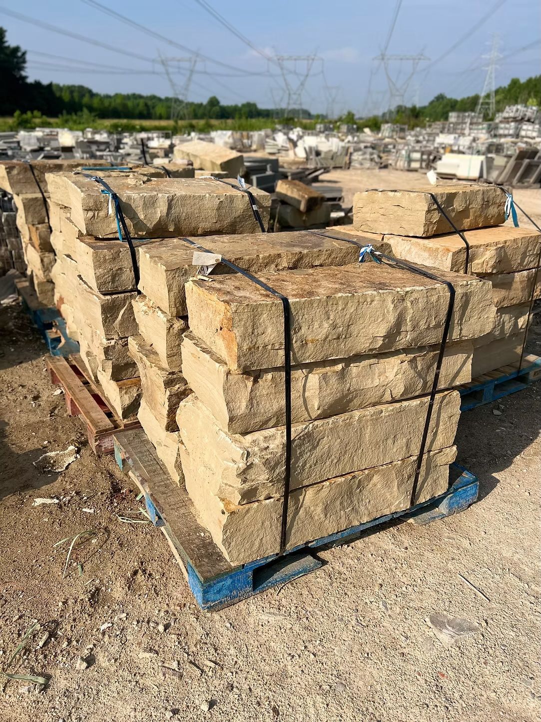 Pallet of rectangular beige stone blocks, outdoors on a gravel lot, with power lines in the background.