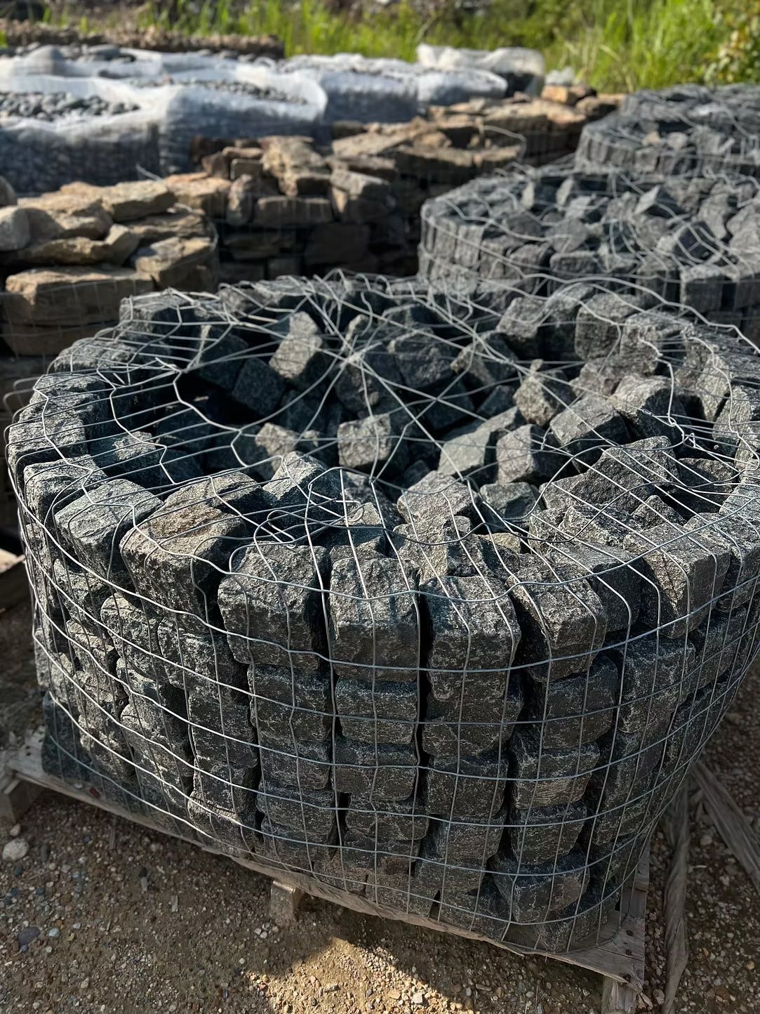 Black square stones in wire cages, stacked on a wooden pallet outdoors.