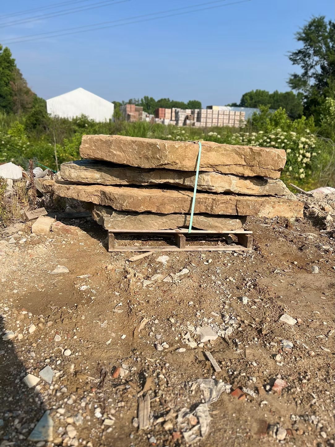 Stack of large, weathered stone slabs secured with green twine on a wooden pallet in a dirt lot.
