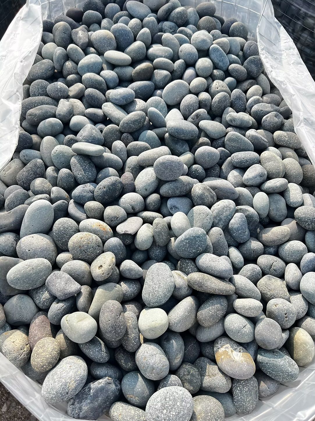 Bag of smooth, gray river rocks for landscaping.