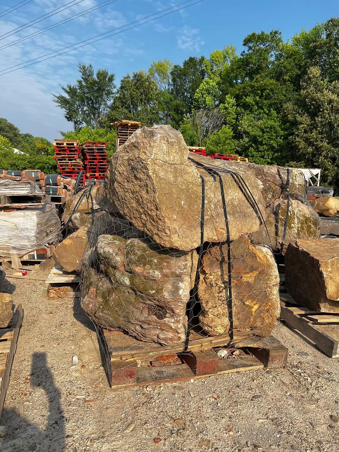 Large, bundled rocks on a wooden pallet, secured with black straps, outdoors under a sunny sky.