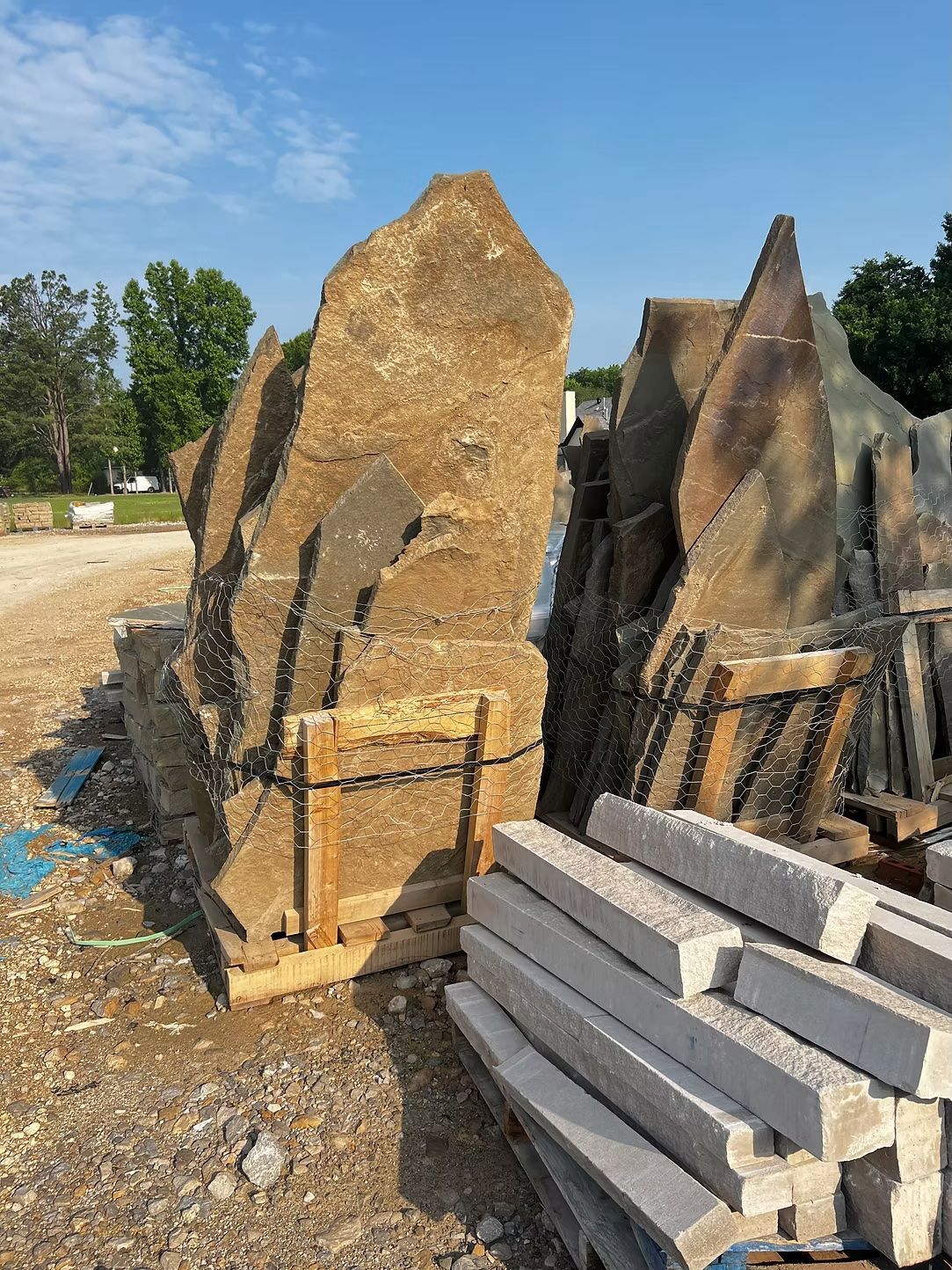 Pile of large, irregular tan-colored rocks secured with wooden supports, next to a stack of concrete pavers.