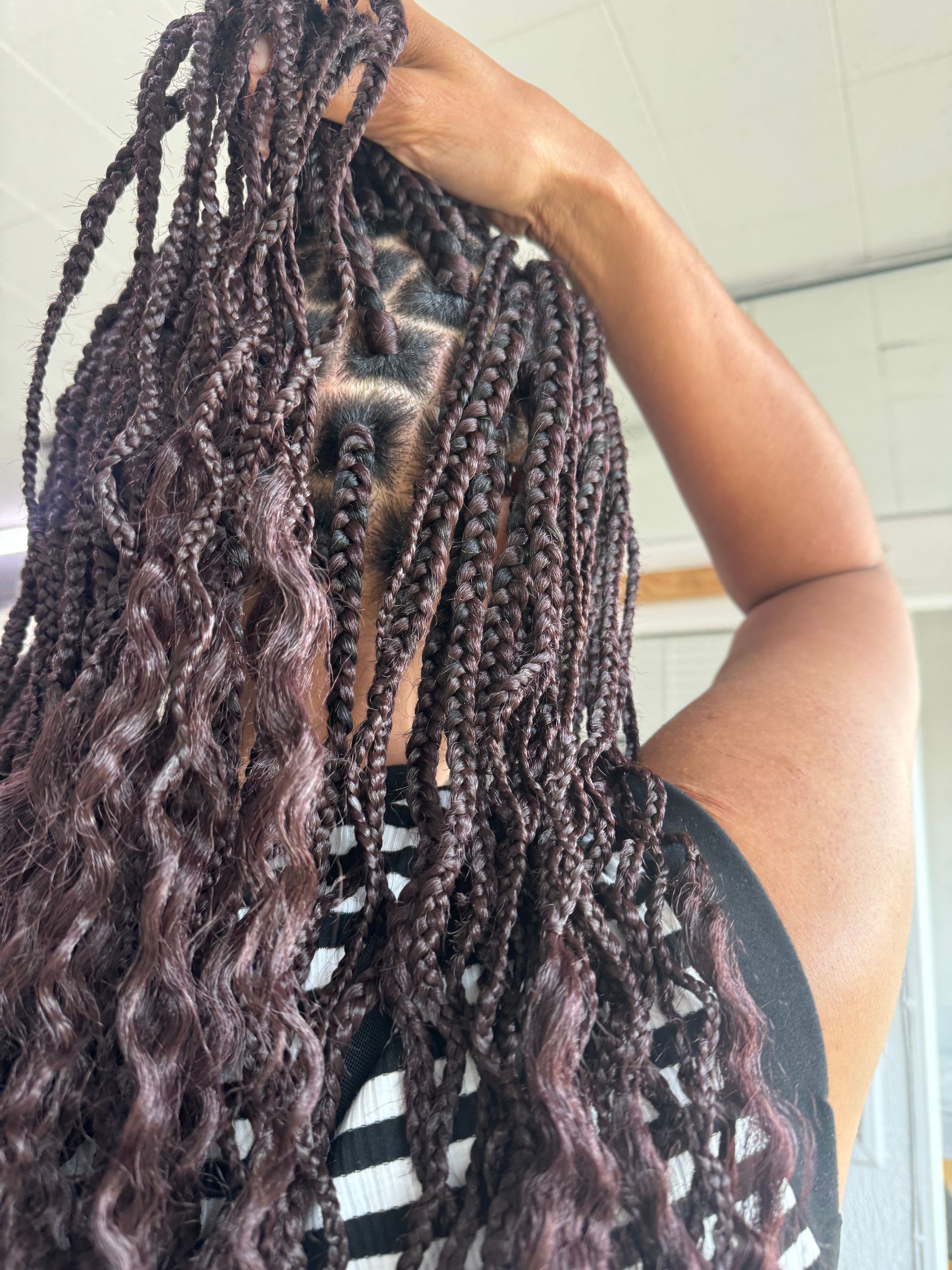 A woman with braids and curly hair is holding her hair in her hand.