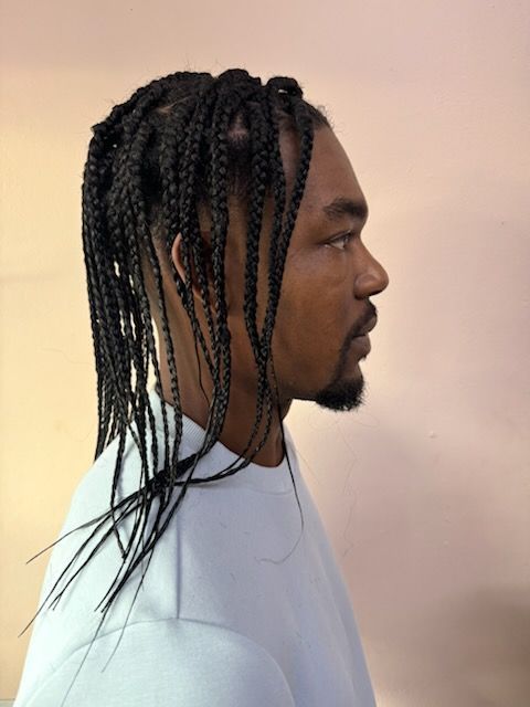 A man with braids and a beard is wearing a white shirt.
