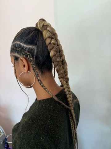 A woman with a braided ponytail and hoop earrings is wearing a green sweater.