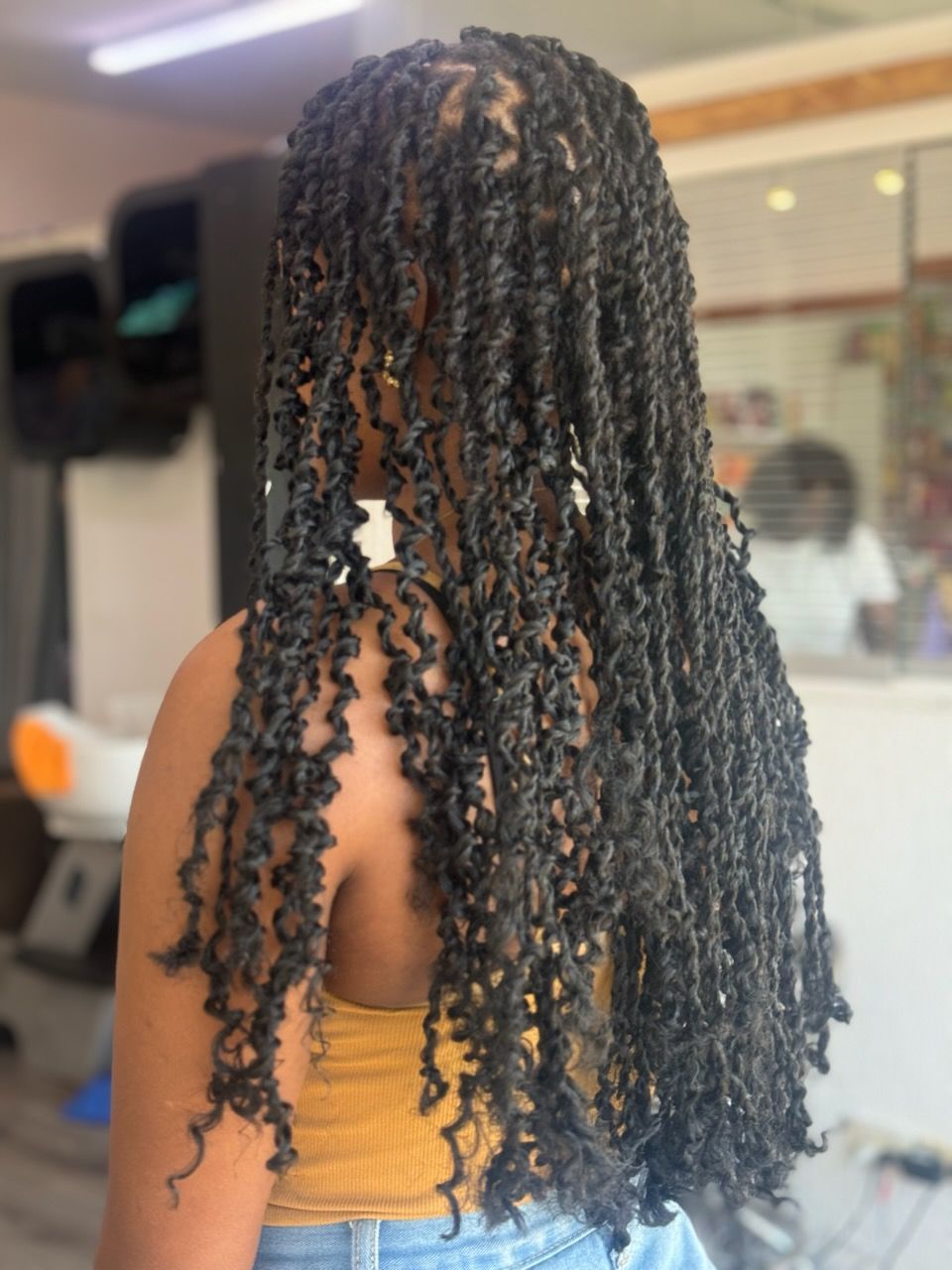 A woman with dreadlocks is wearing a yellow tank top and blue jeans.