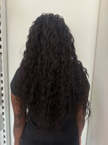 A woman with long curly hair is standing in front of a white wall.
