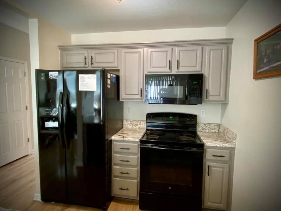 A kitchen with a black refrigerator , stove , and microwave.