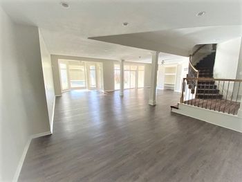 A large empty room with hardwood floors and stairs in a house.