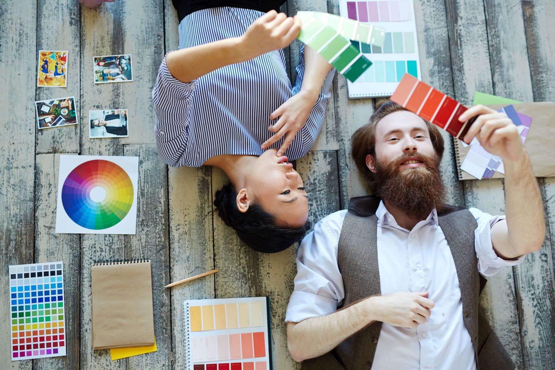 A man and a woman are laying on the floor looking at paint samples.