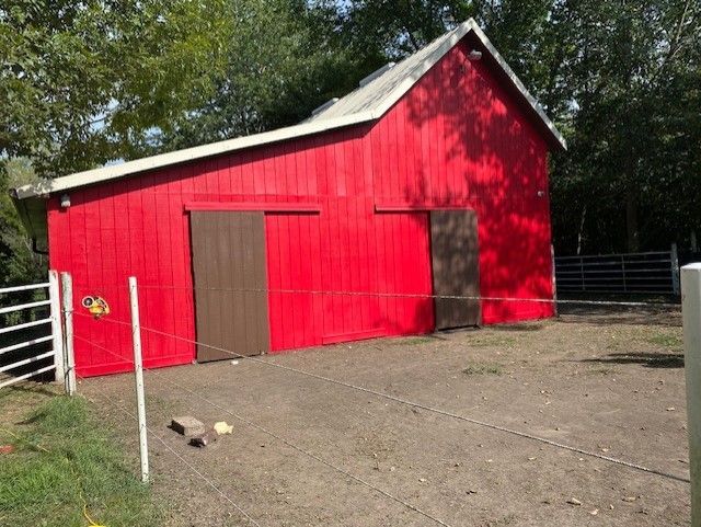 A red barn with a fence around it and trees in the background.