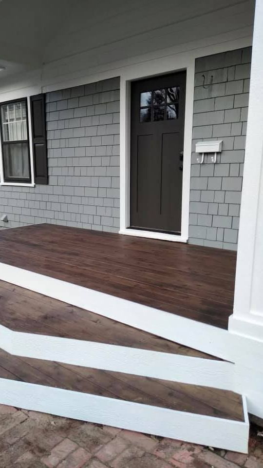 The front porch of a house with a wooden floor and a white railing.