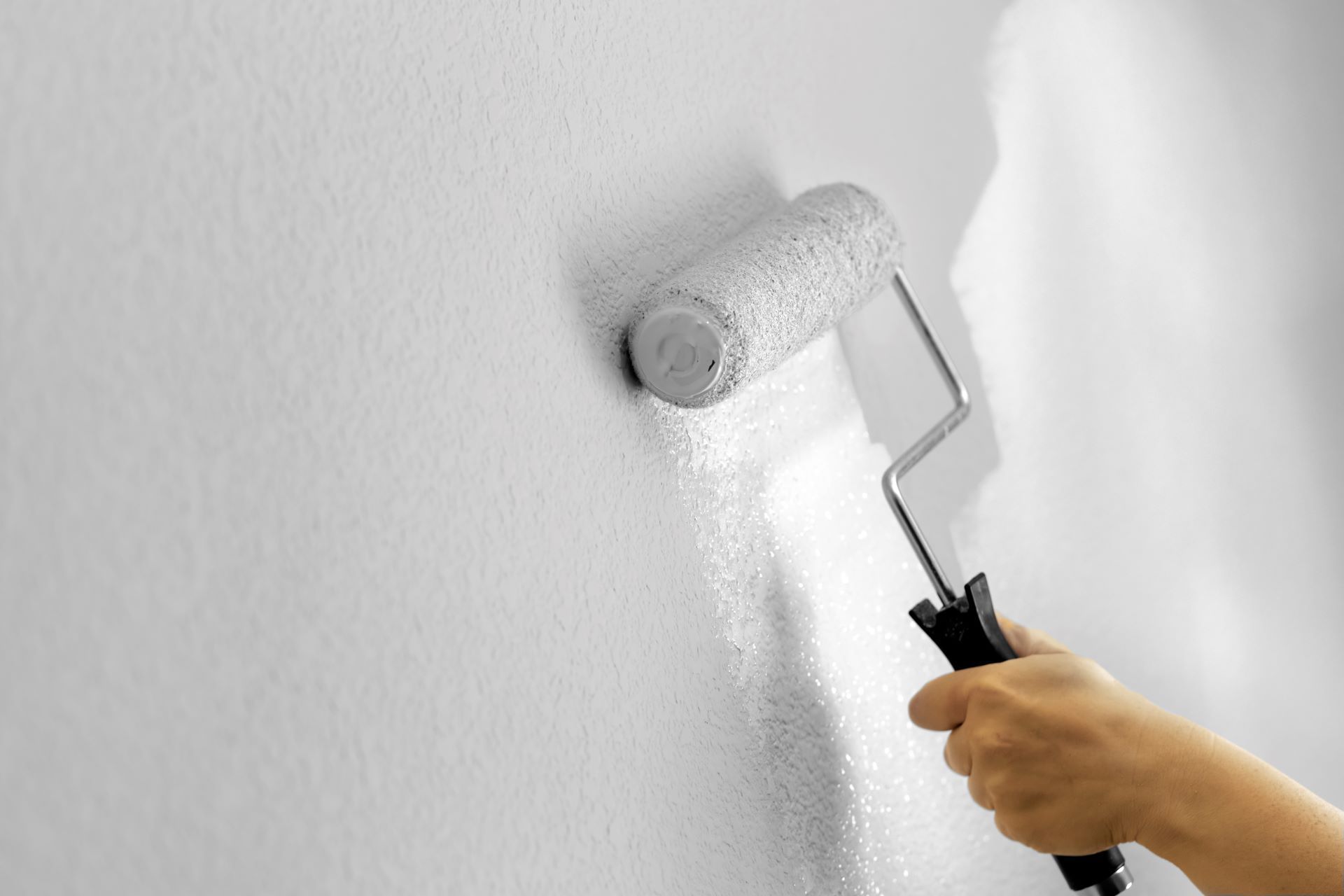 A person is painting a wall with a paint roller. White paint.