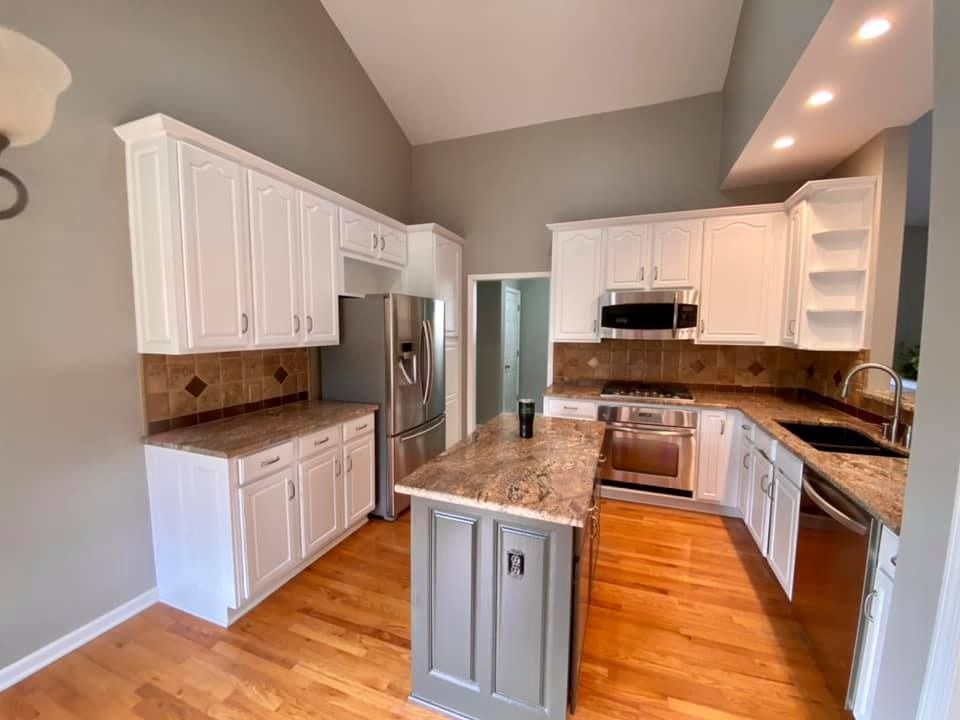 A kitchen with white cabinets , granite counter tops , stainless steel appliances and a large island.