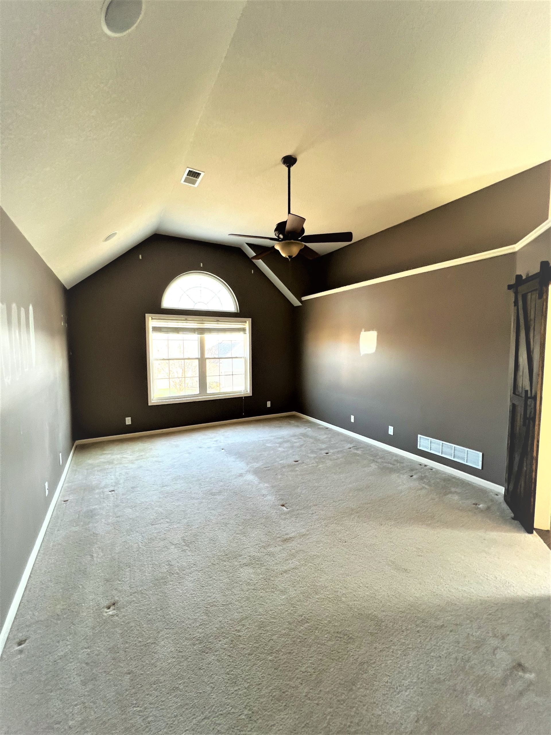 An empty living room with a ceiling fan and a large window.
