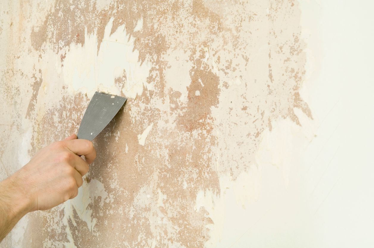 Person stripping wallpaper by hand using a special tool - preparing walls for painting.