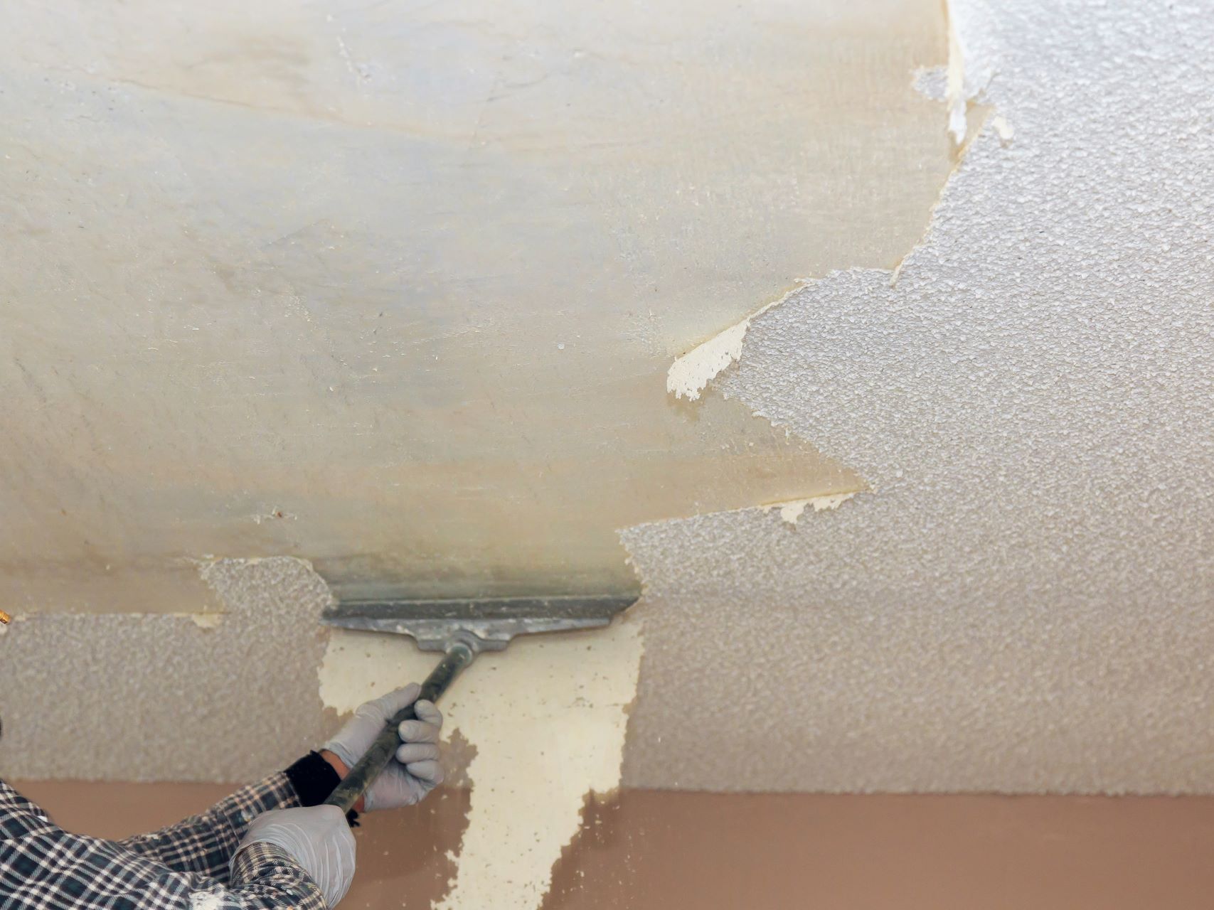 A person is removing wallpaper from a ceiling with a spatula.