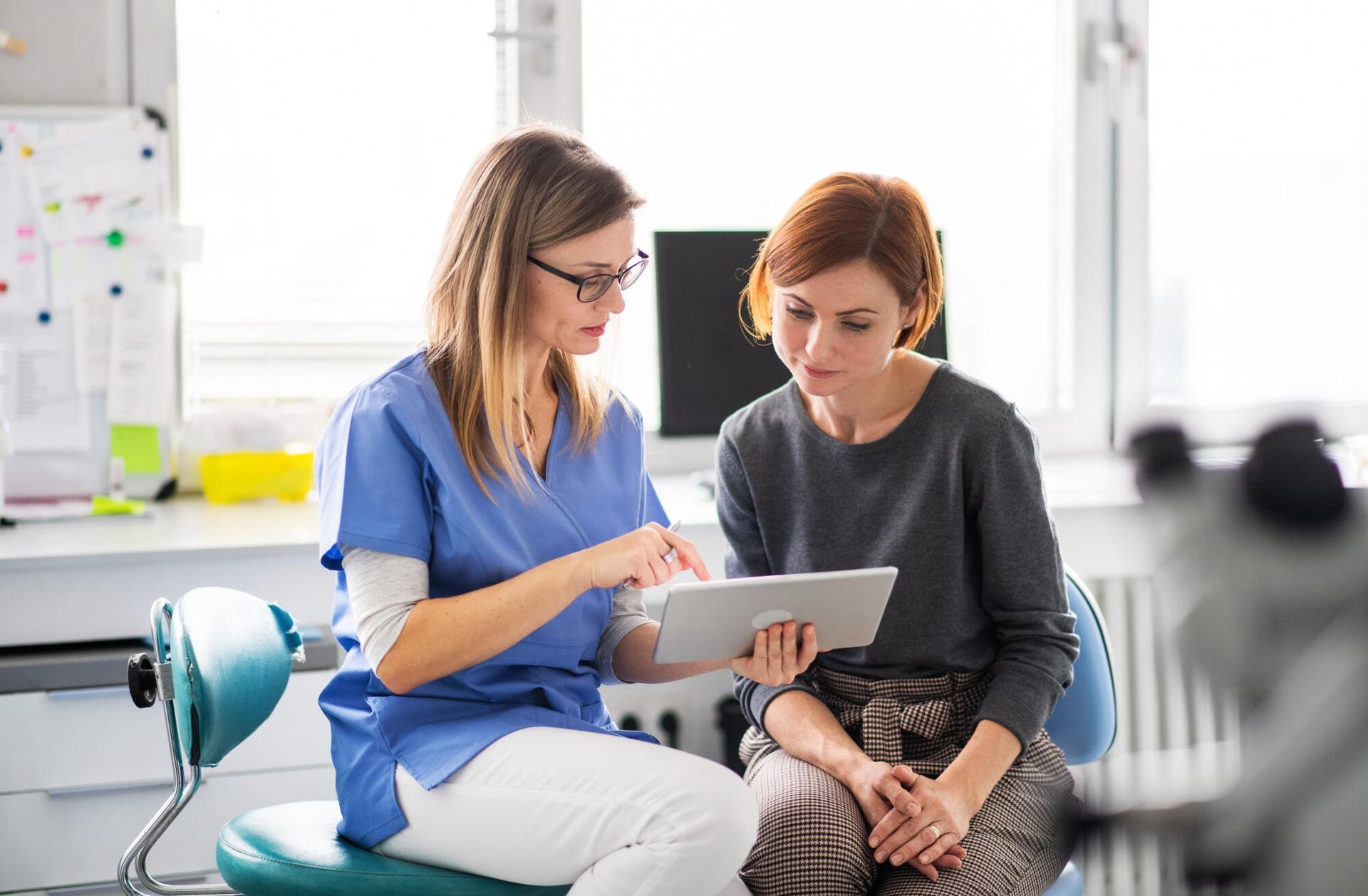 A nurse is talking to a patient while looking at a tablet.