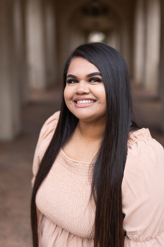 A woman with long hair is smiling for the camera in a hallway.