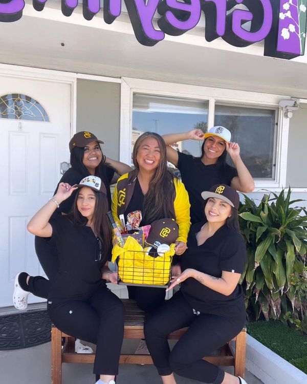 A group of women are sitting on a bench in front of a house holding a basket.