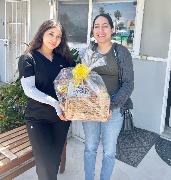 Two women are standing next to each other holding a basket with a yellow flower on it.