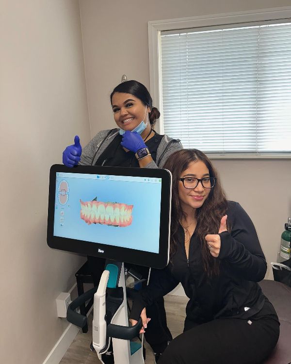 Two women are giving a thumbs up in front of a computer monitor.