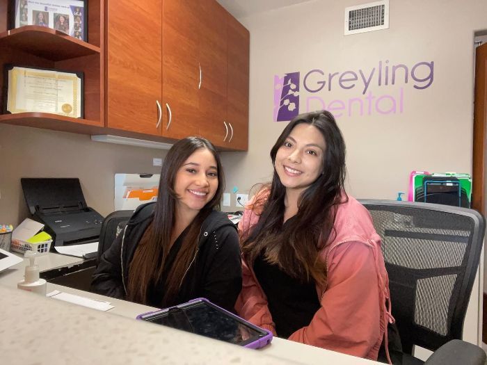 Two women are sitting at a desk in a dental office.