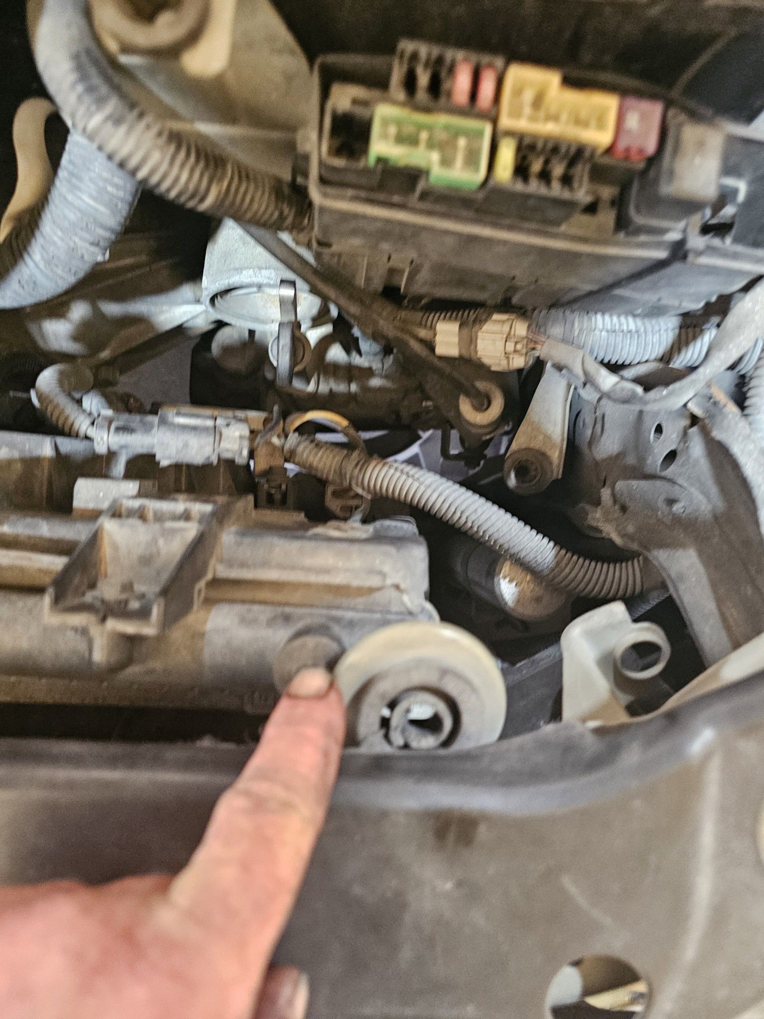 A person is pointing at a fuse box on a car engine.