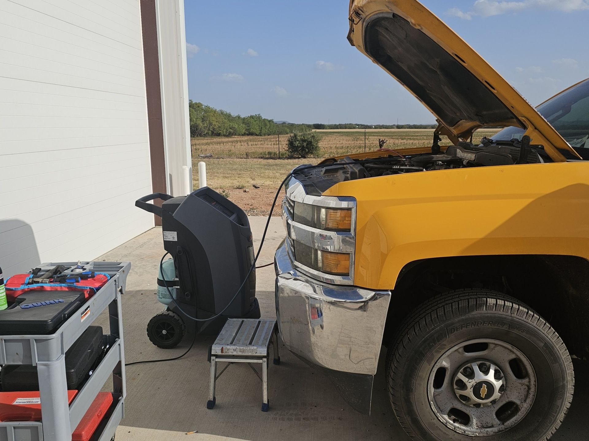A yellow truck with the hood up is being charged