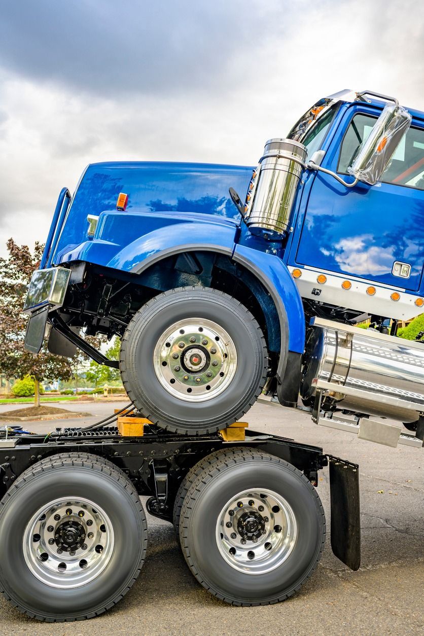 A blue semi truck is sitting on top of a trailer.