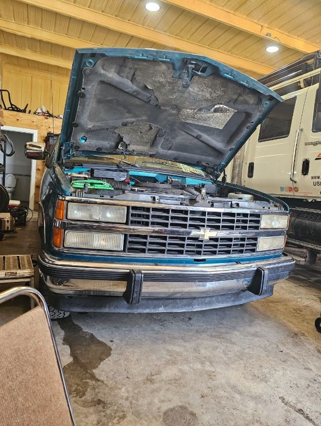 A blue chevrolet truck with the hood up is parked in a garage.