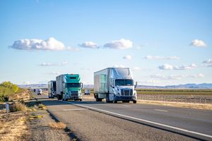 A row of semi trucks are driving down a highway.