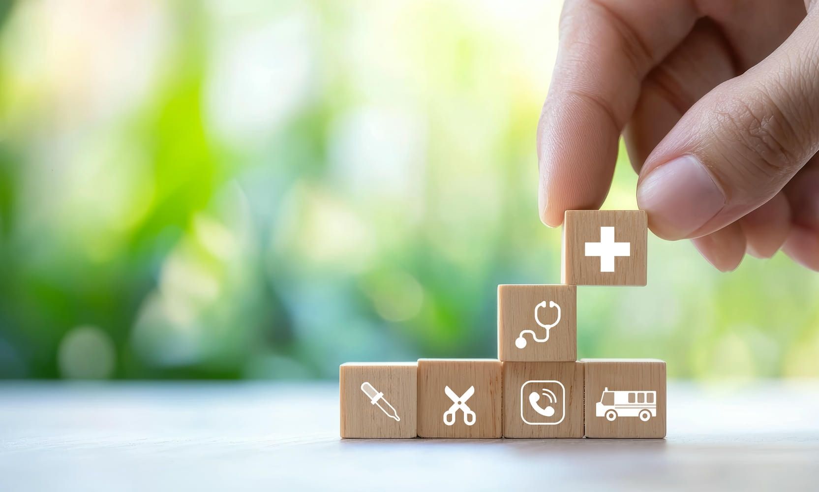 A hand is stacking wooden blocks with medical icons on them.
