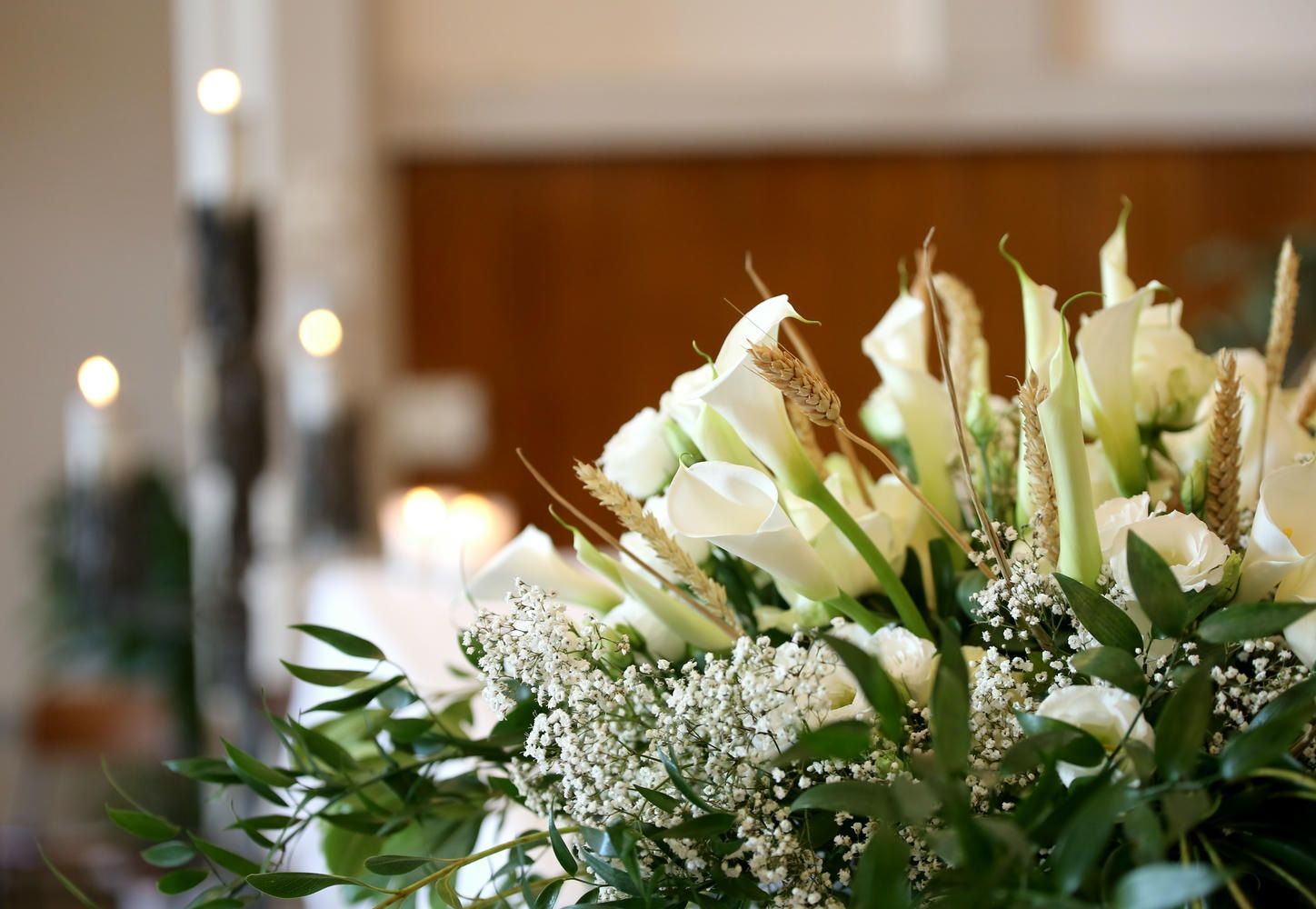 A bouquet of white flowers with baby 's breath and candles in the background