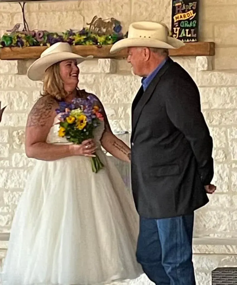 A bride and groom are standing next to each other in front of a fireplace.