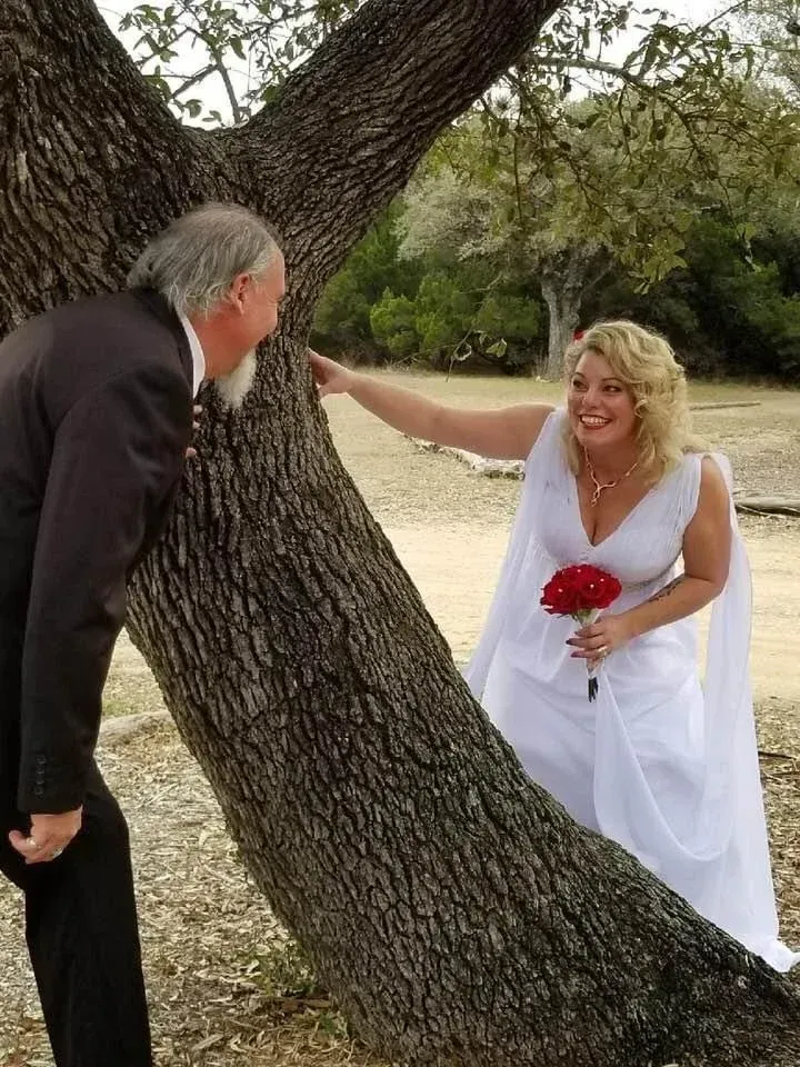 A bride and groom standing next to a tree