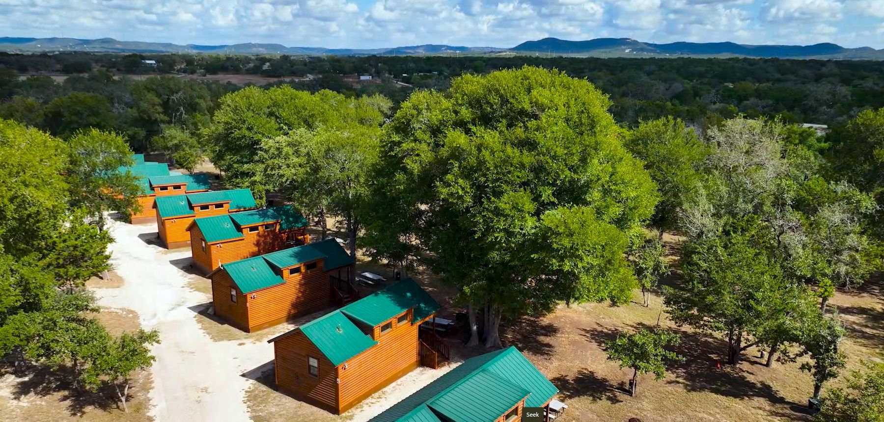 An aerial view of a row of wooden cabins surrounded by trees.