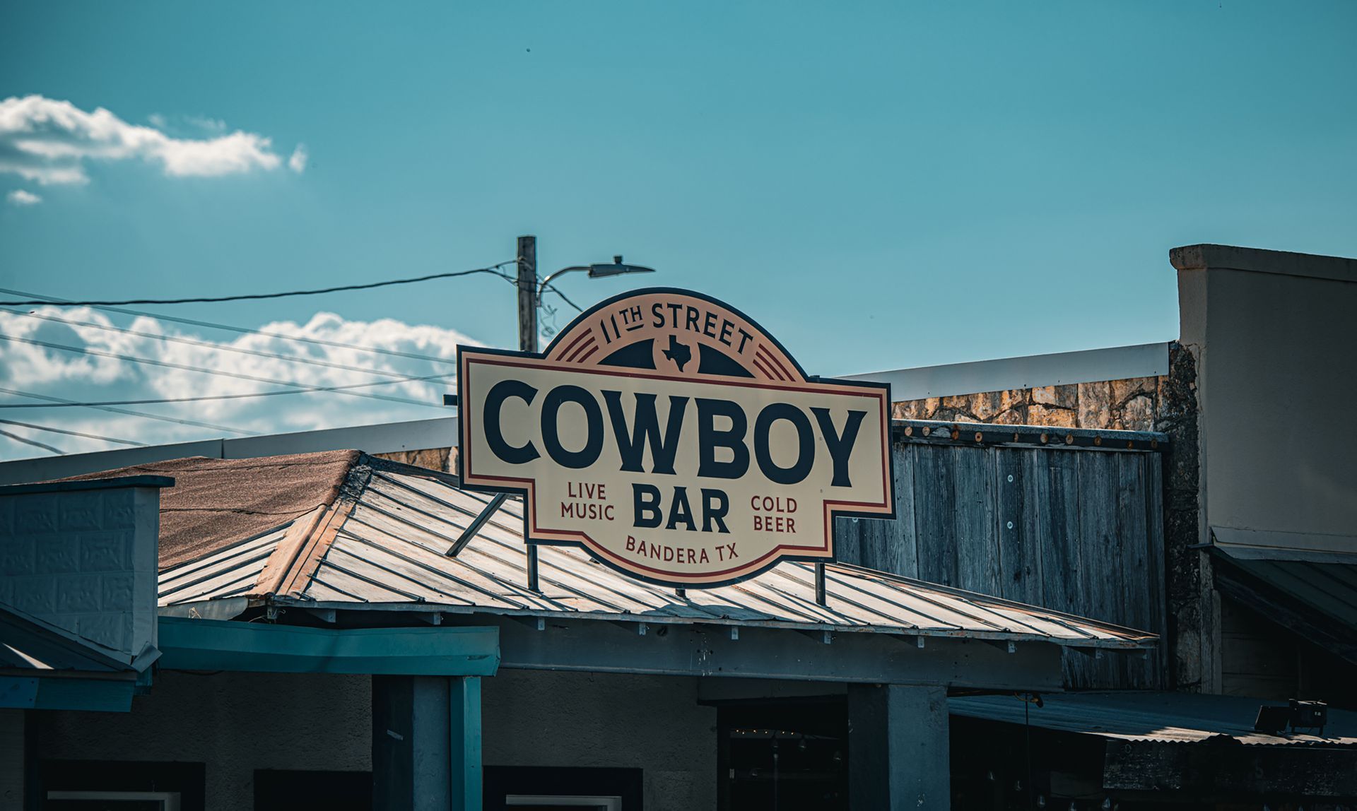 A cowboy bar sign is hanging from the roof of a building.