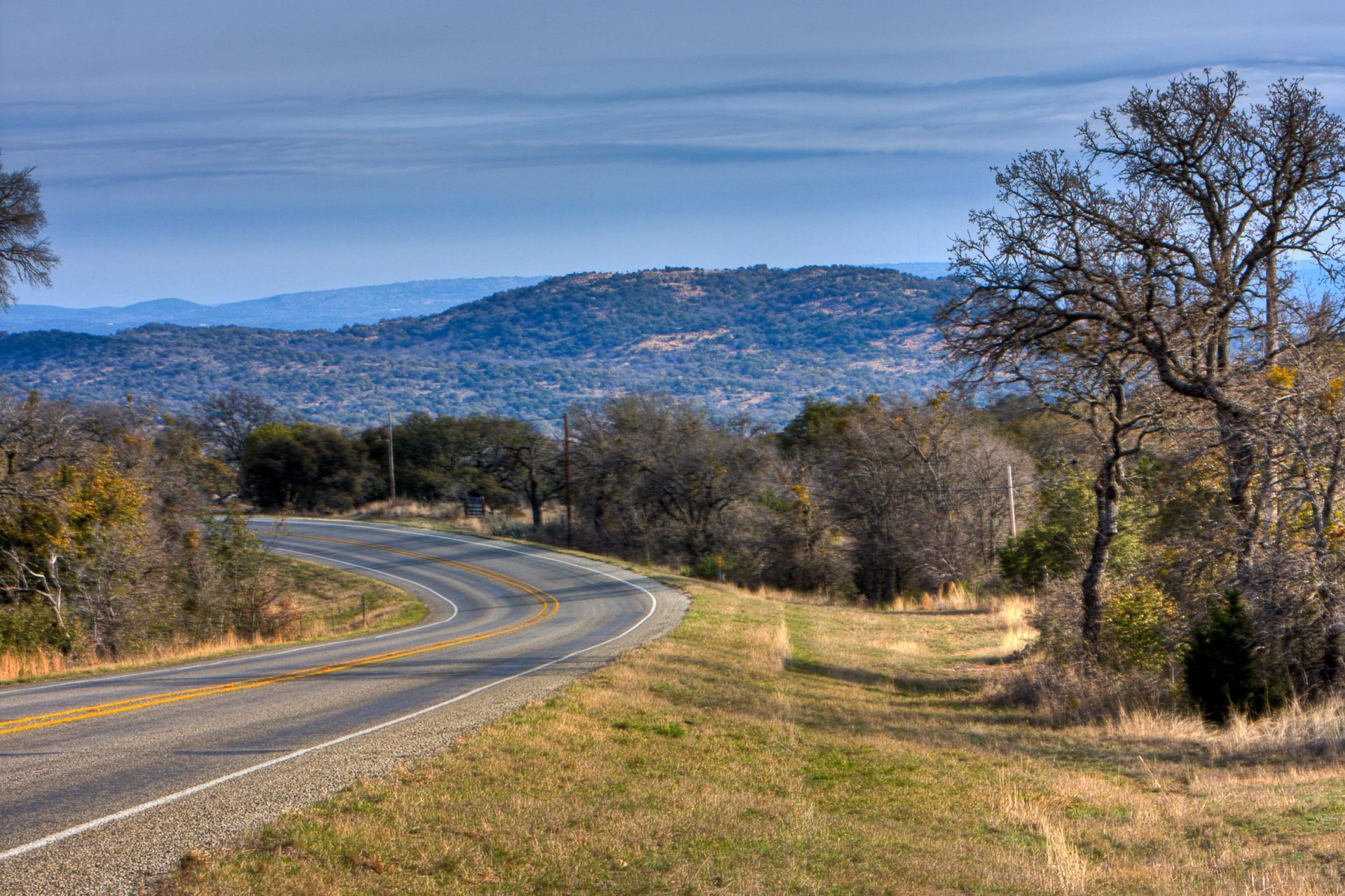 A curvy road with trees on both sides and mountains in the background.