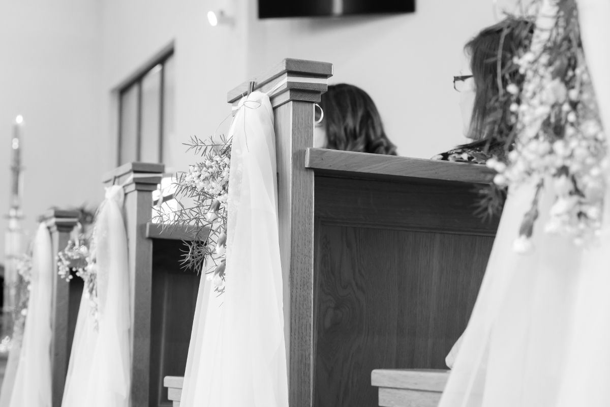 A black and white photo of a bride and groom sitting in a church.