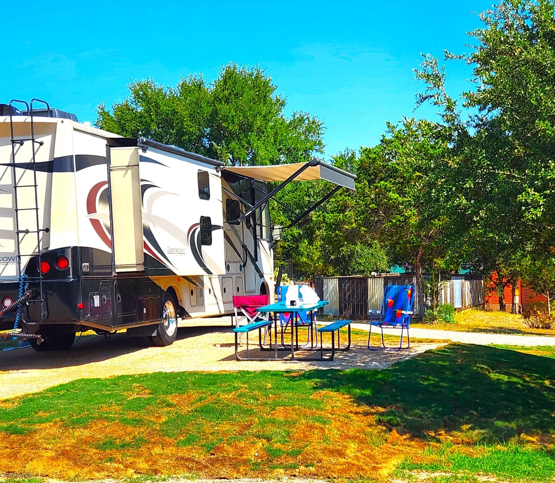 A rv is parked in a campground with a picnic table and chairs.