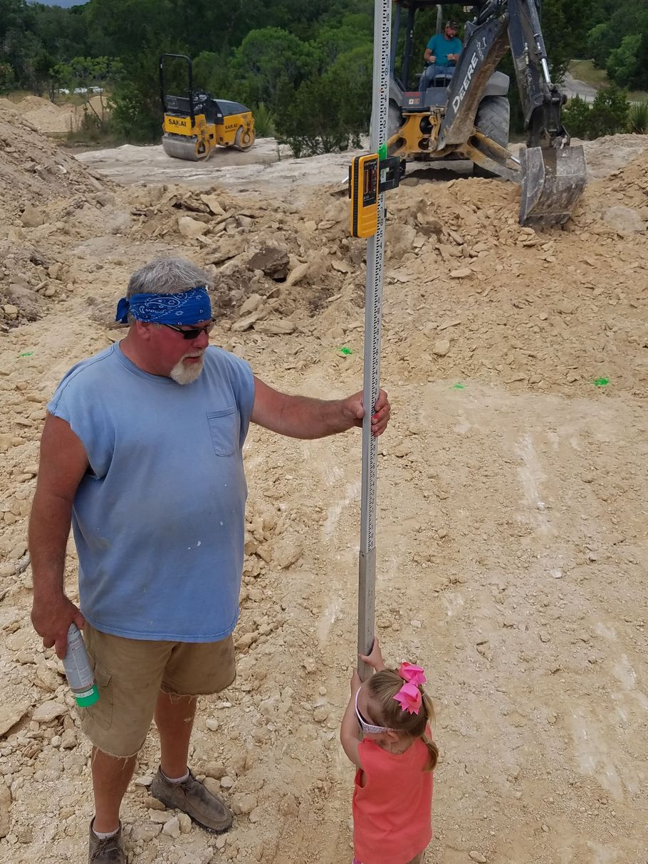 Man in blue shirt and child in red shirt holding a measuring rod at a construction site