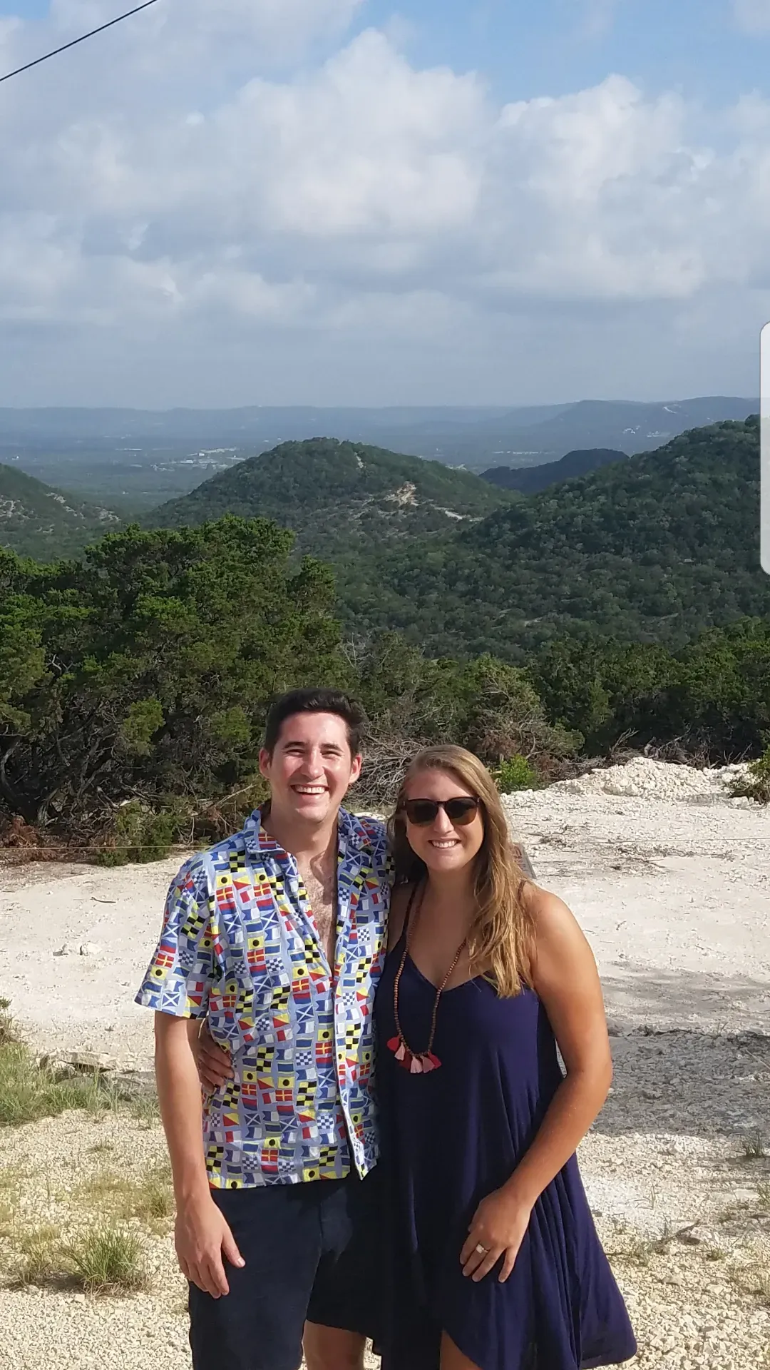 A man and a woman are standing next to each other on top of a hill.