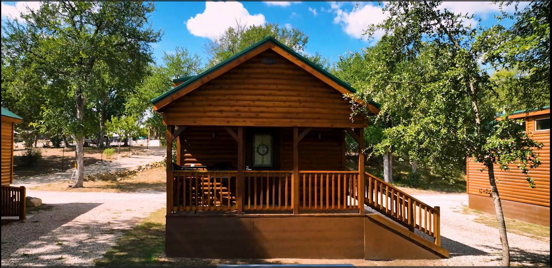 A small wooden cabin with a green roof is surrounded by trees.