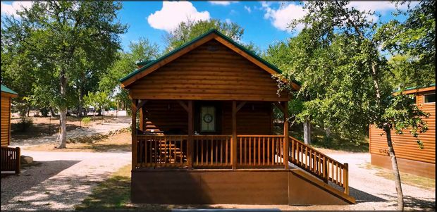 A small wooden cabin with a green roof is surrounded by trees.