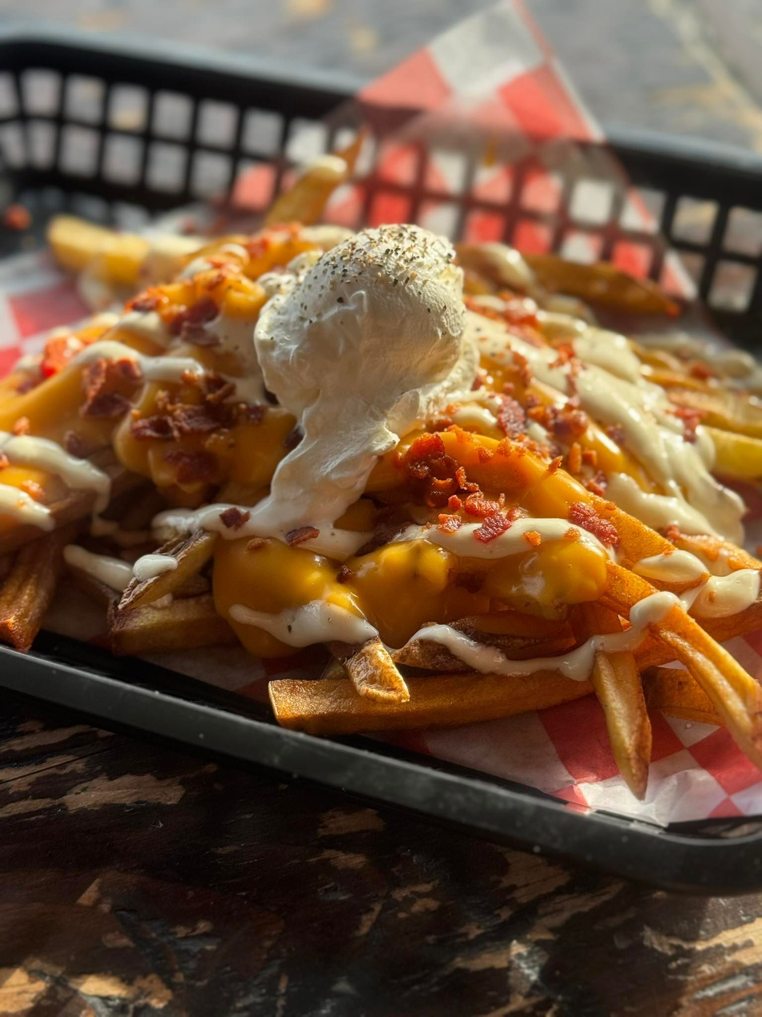 A basket of french fries with cheese and bacon on a table.