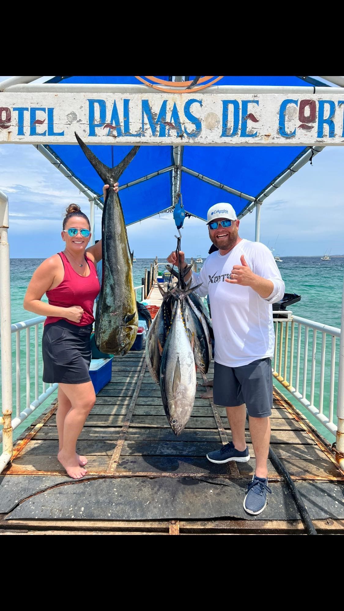 A man and a woman are standing on a dock holding fish.